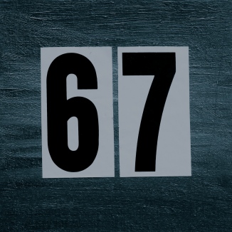 grey painted square background, in the center, large adhesive black numbers 6 and 7 almost filling the space. The numbers have a white rectangular background